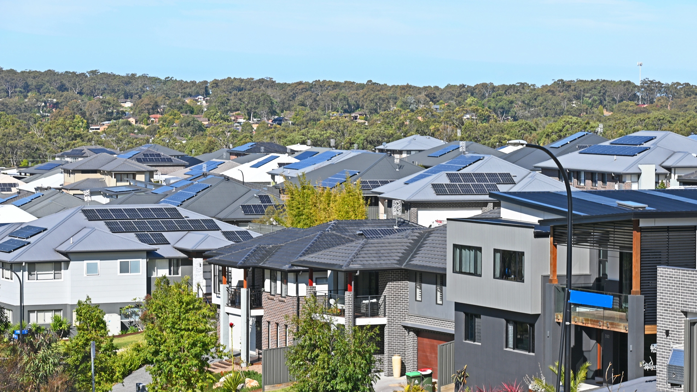 Aerial view of a modern Australian suburban neighborhood with solar panels on rooftops, surrounded by lush greenery