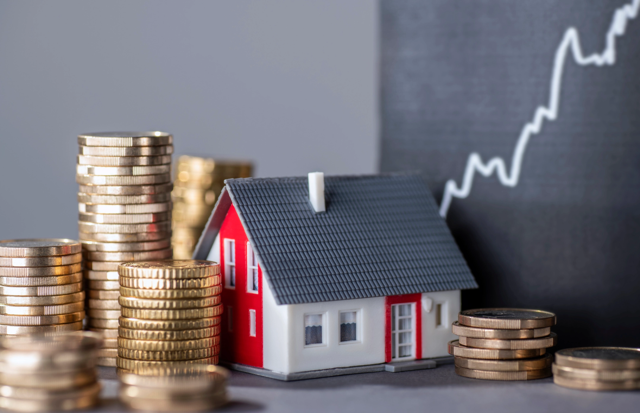 Stacks of coins next to a small house model with a rising graph in the background, symbolizing investment home loans and financial growth